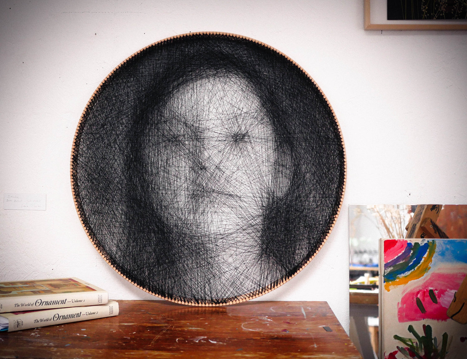 Stringading String Art lehnt an einer Wand. Das Motiv ist eine junge Frau